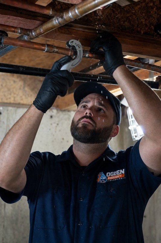 A plumber cutting out a split section of copper supply pipe in a basement