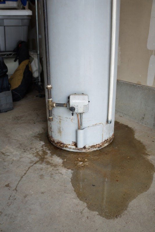 A leaking gas water heater with water spreading across a garage floor